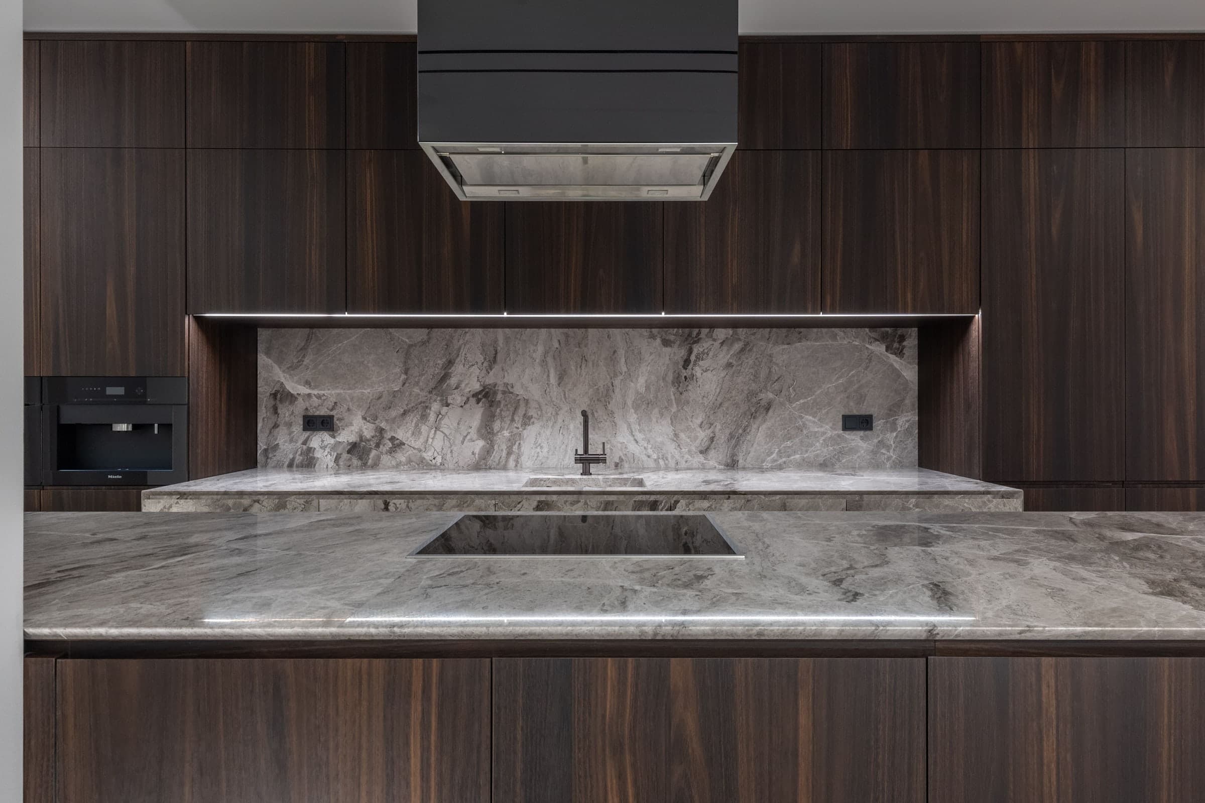 Dark walnut kitchen cabinetry under a stone slab backsplash