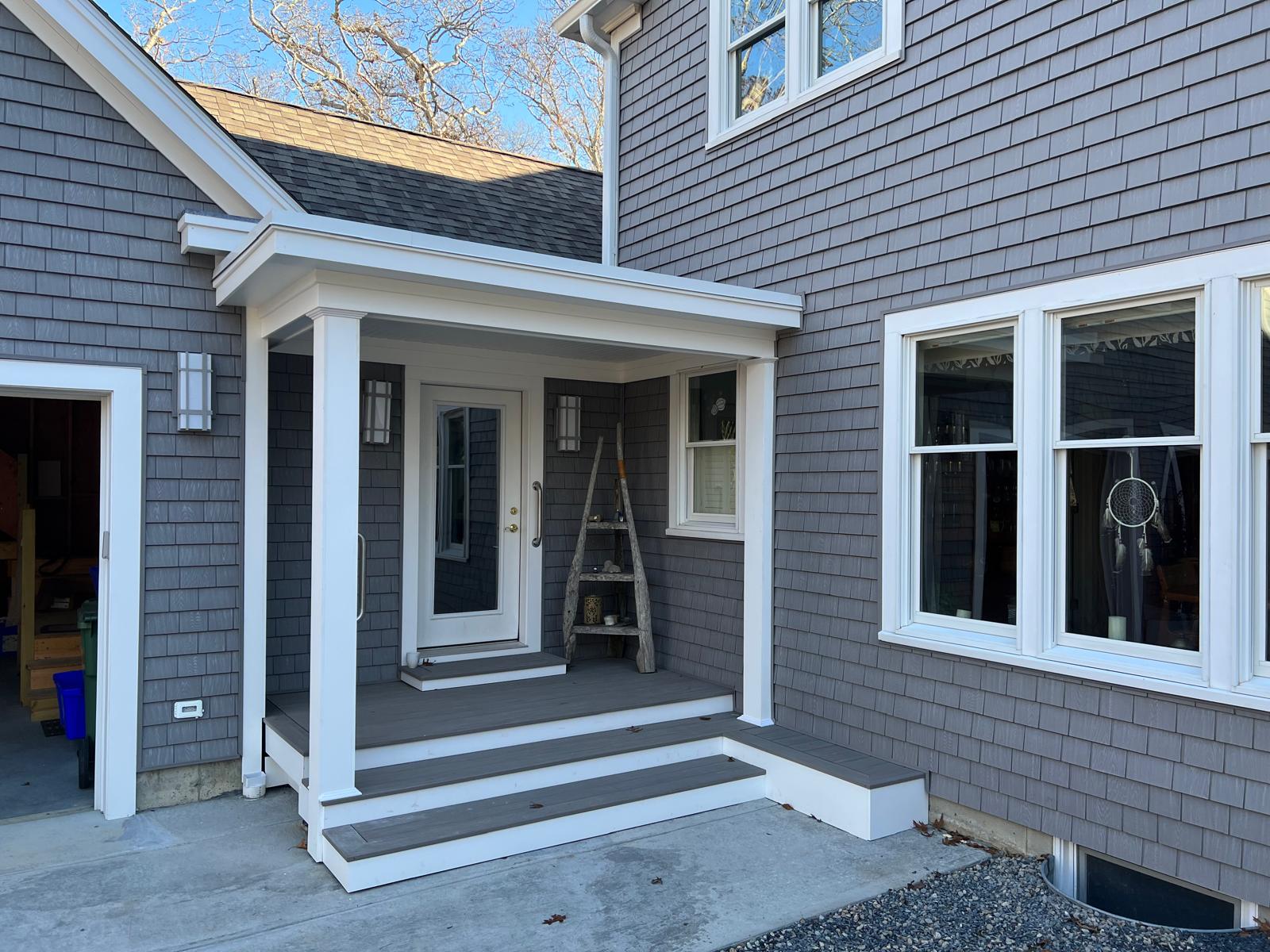 Grey cedar-shingle facade with a white-columned covered entry and large windows