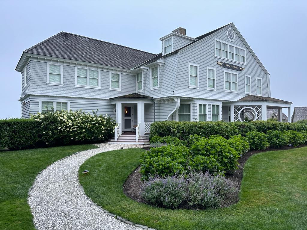Large white cedar-shingle home with a curved gravel walkway and clipped hedges